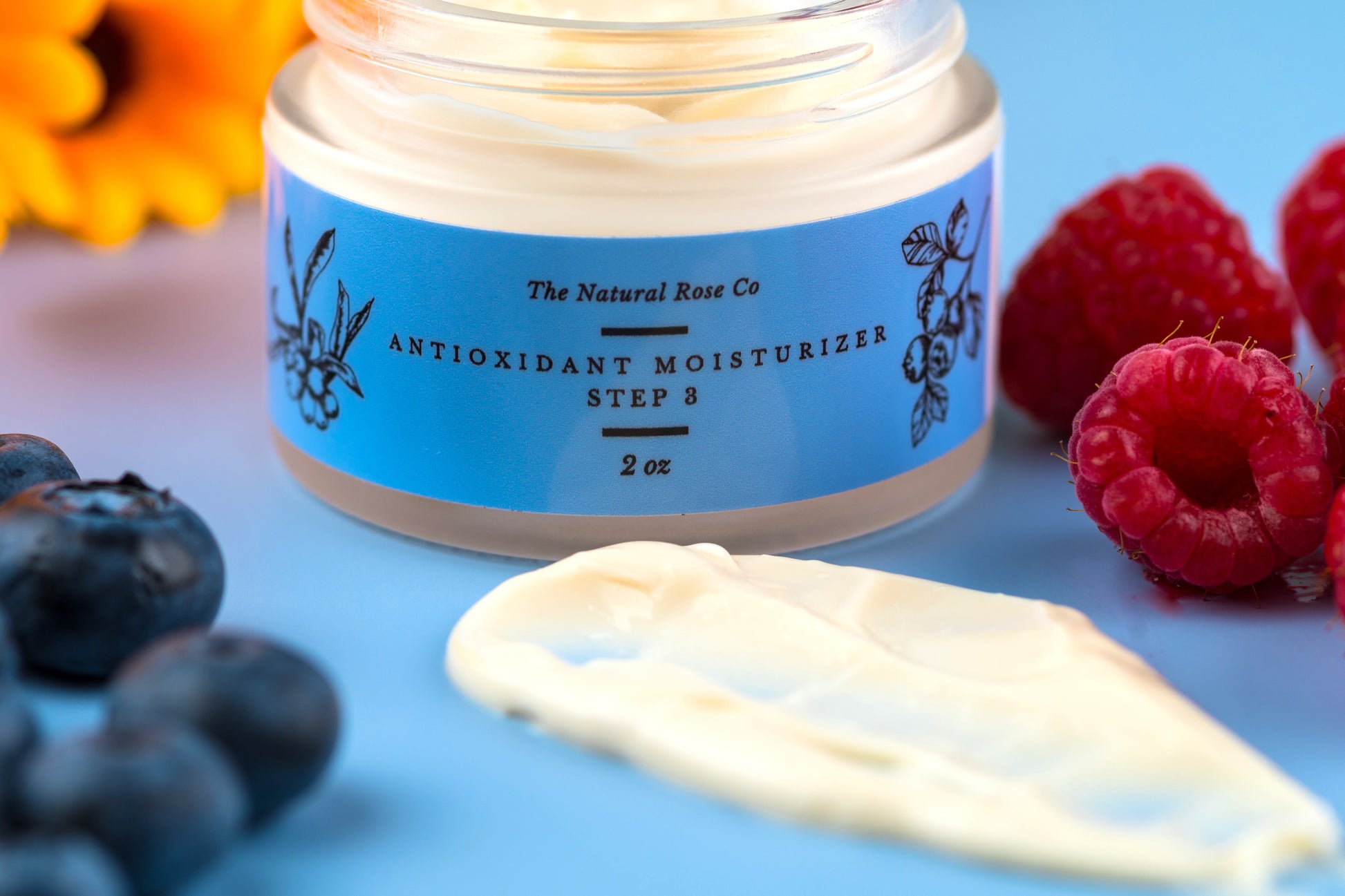 The Natural Rose natural skincare antioxidant cream in blue jar with cream and fresh berries on blue background